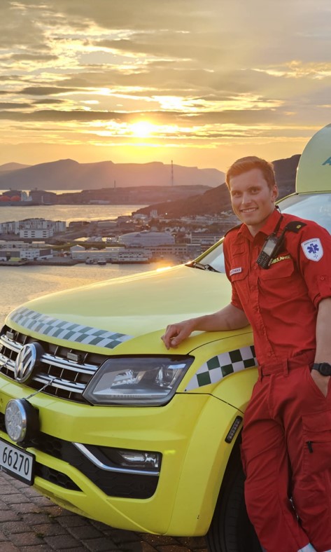 En mann som står ved siden av en gul sportsbil med en by i bakgrunnen