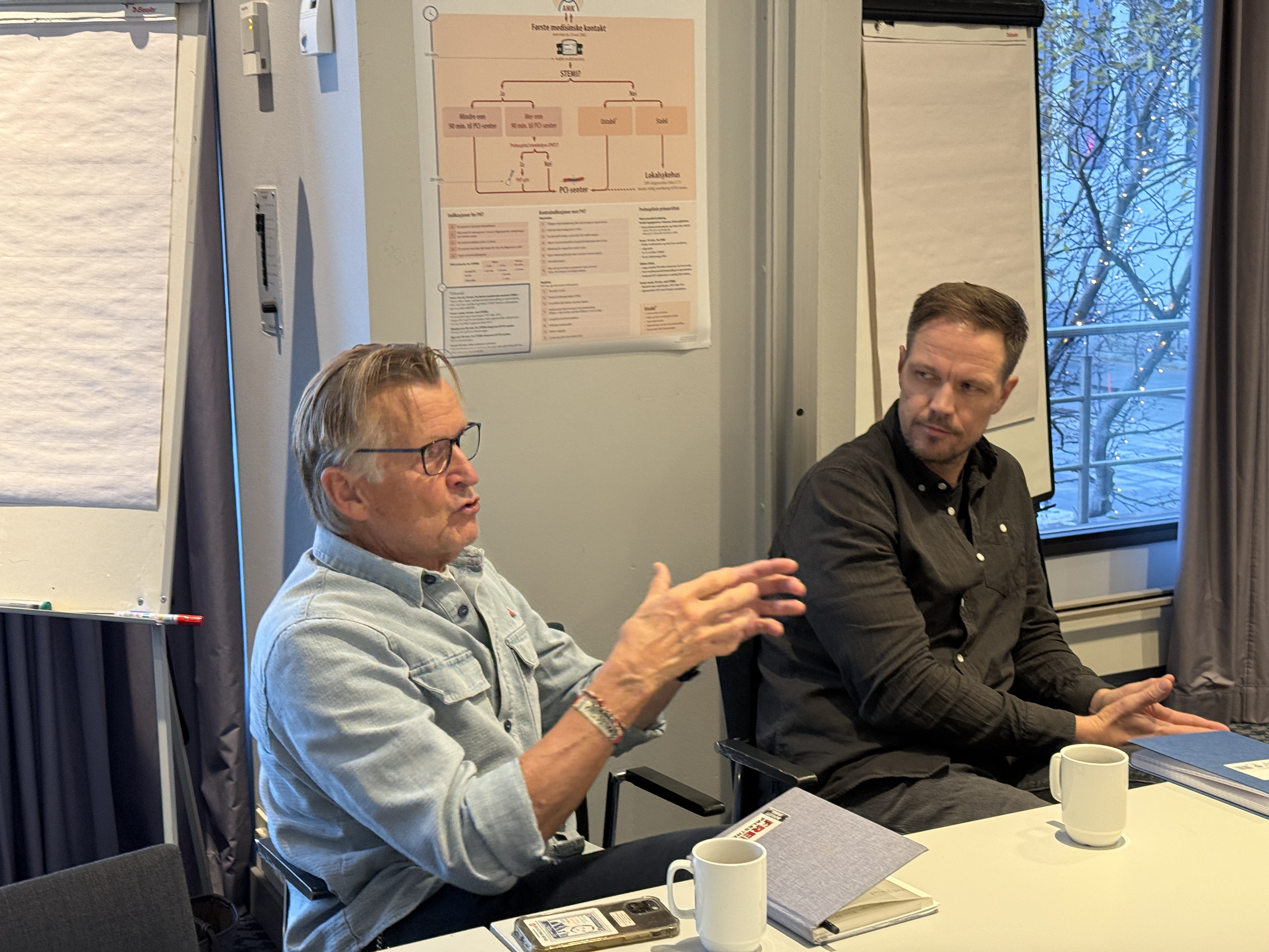 Et par menn som sitter ved et bord og snakker