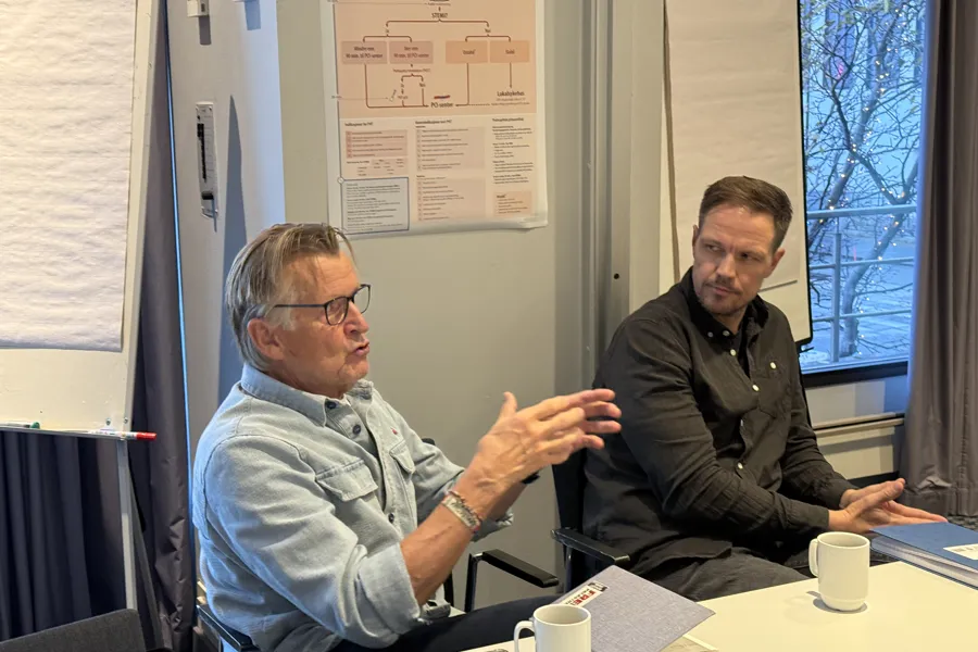 Et par menn som sitter ved et bord og snakker